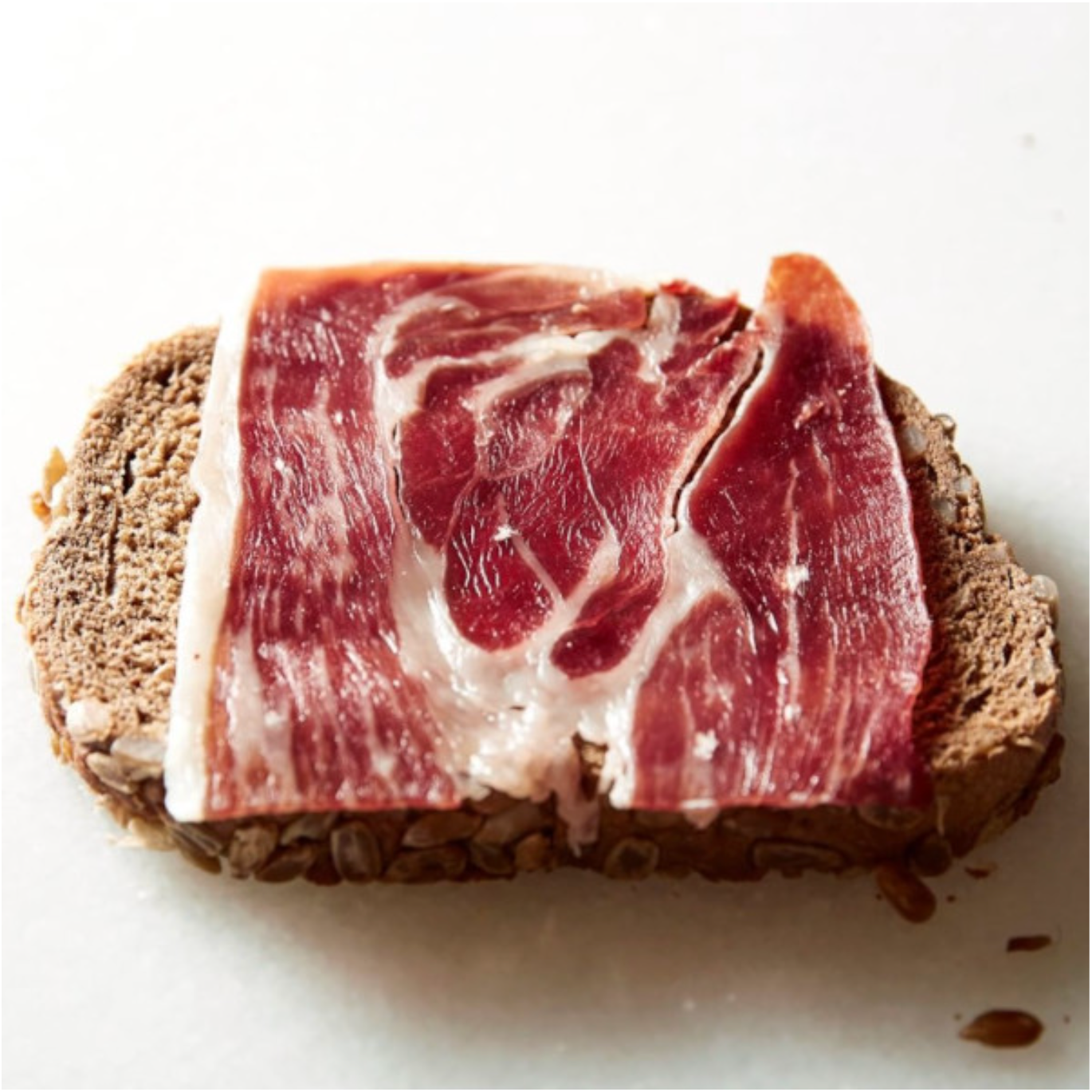 A slice of Marcos dry-cured Iberico pork ham on a piece of bread, showcasing its marbling and premium quality.