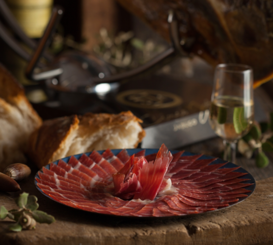 A delicately arranged plate of Cinco Jotas 5J Iberico Jamon, paired with bread and wine in the background.