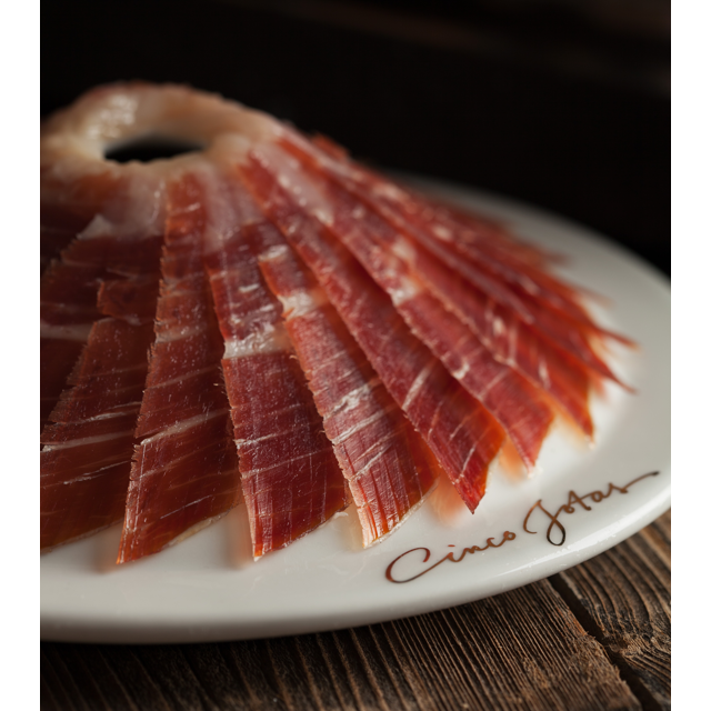 Thinly sliced Cinco Jotas 5J Iberico ham arranged beautifully on a white plate.